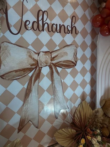 A close-up of the custom-designed backdrop for the naming ceremony. The large bow graphic and elegant script add a touch of sweetness to the sophisticated boho theme.