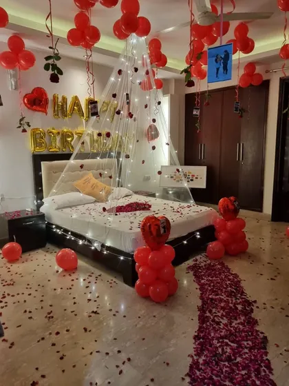 A look at our classic romantic birthday decoration. We turn a bedroom into a lover's paradise with a ceiling full of red balloons, a fairy light canopy over the bed, a path of rose petals, and even your personal photos hanging from the balloons.