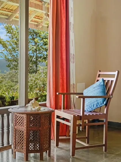 A quiet corner on the veranda with a view of the lush green valley. The carved wooden table and colorful curtains create a perfect spot for a morning cup of tea.