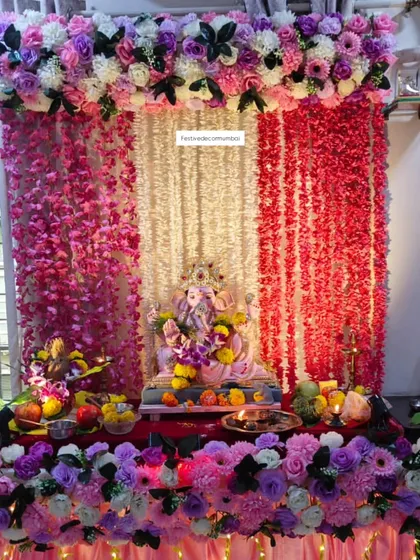 This vibrant Ganpati mandap features a backdrop of cascading pink, purple, and white floral strings. The dense arrangement of flowers at the top and bottom frames the idol beautifully.