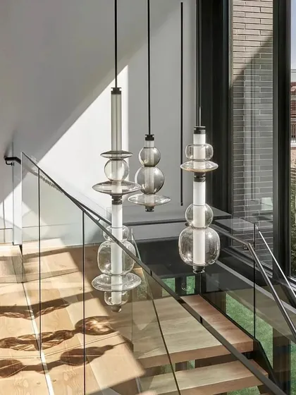 A trio of Luna Kaleido pendants cascades down a modern staircase, creating a dramatic vertical feature and casting beautiful shadows on the surrounding walls.