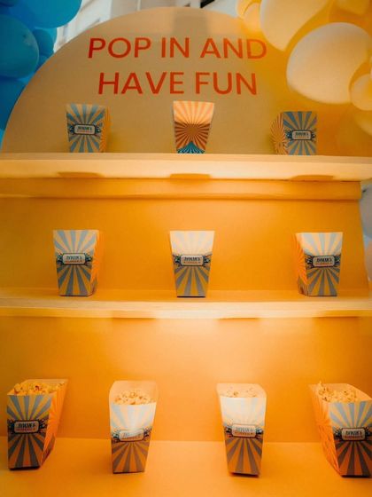 A "Pop in and have fun" popcorn station at a carnival-themed party. The custom-built yellow shelf is designed to hold individual popcorn boxes for guests.