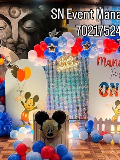 A vibrant Mickey Mouse clubhouse theme for Manvik's first birthday. This large setup includes multiple backdrops, character cutouts, a picket fence, and a colorful balloon arch.