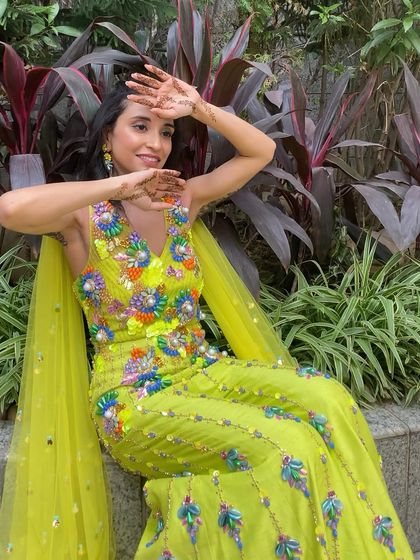 A full view of the bride's vibrant mehendi look. The colorful outfit is balanced with fresh, glowing makeup and a simple, elegant hairstyle.