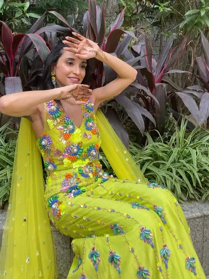 A full view of the bride's vibrant mehendi look. The colorful outfit is balanced with fresh, glowing makeup and a simple, elegant hairstyle.
