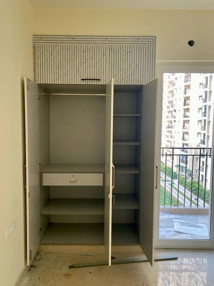 The inside of the three-shutter wardrobe, showing the spacious interior with a hanging rod, shelves, and a lower drawer.