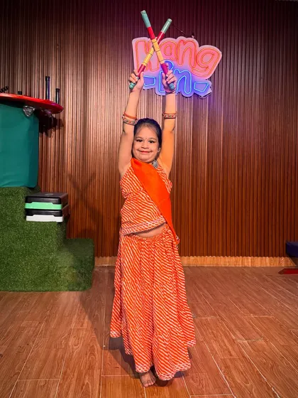 Dressed in a vibrant orange bandhani lehenga, this student holds her dandiya sticks high. This photo highlights the colorful and festive atmosphere of our Navratri dance workshops.
