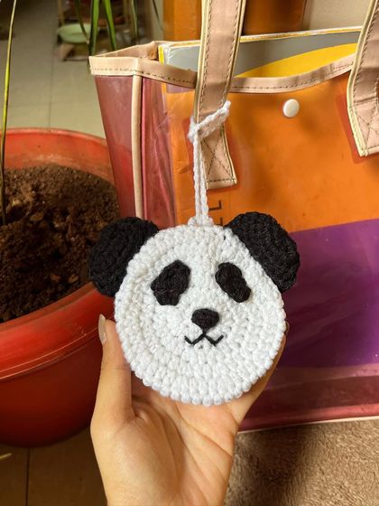 A hand holding the crochet panda pouch, giving a sense of its size and soft texture.