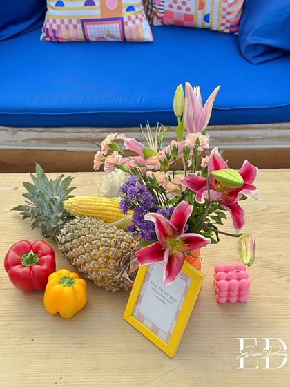 A close-up of a centerpiece combining flowers with fresh corn and pineapple, illustrating the unconventional use of natural elements.