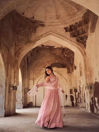 A wide-angle shot capturing the grandeur of the location and the elegance of the pink lehenga. The architectural arches frame the model, creating a sense of scale and romance for this ethnic wear campaign.