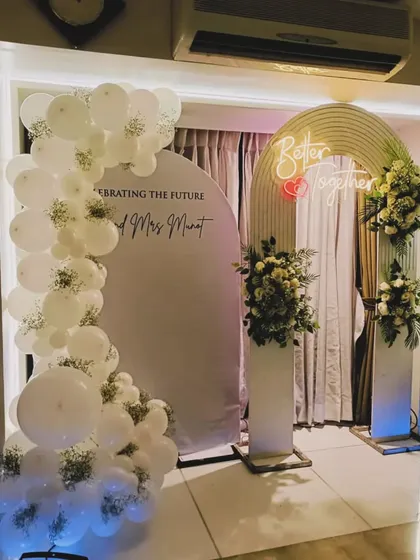A beautiful white-themed engagement or party backdrop. The setup includes a balloon arch, a "Better Together" neon sign, and fresh floral arrangements for a classic look.