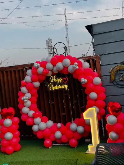 Another angle of the vibrant red and silver balloon ring, perfect for anniversary photos. The neon sign adds a warm glow to the outdoor setting.