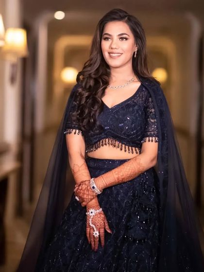 A glamorous engagement look in a navy blue lehenga. The makeup is sophisticated and polished, with soft smokey eyes that complement the deep color of the outfit.