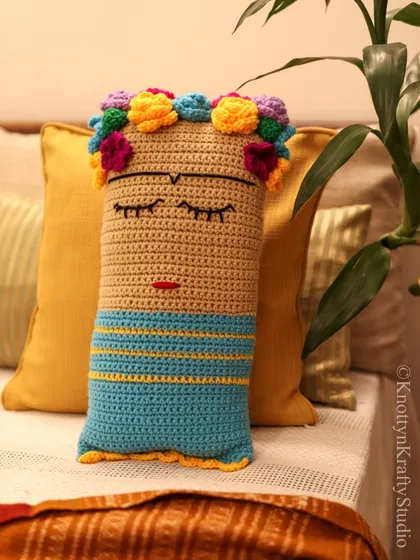 The Frida cushion resting against a warm yellow pillow, showing its versatility with different color palettes. The handmade quality adds a unique, personal touch to home decor.