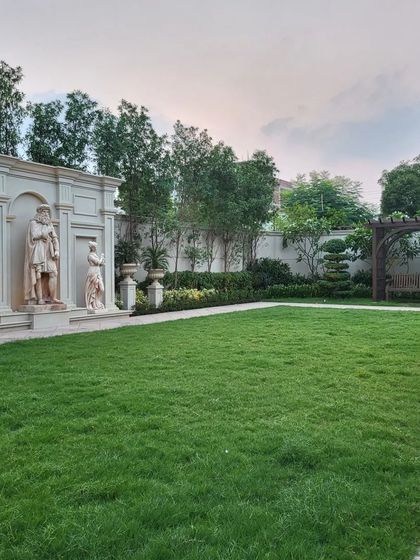 A classical feature wall with magnificent sculptures stands at the edge of a vast lawn in a Gurugram farmhouse. This composition, paired with a wooden swing pergola, evokes a sense of timeless European elegance and provides a stunning backdrop.