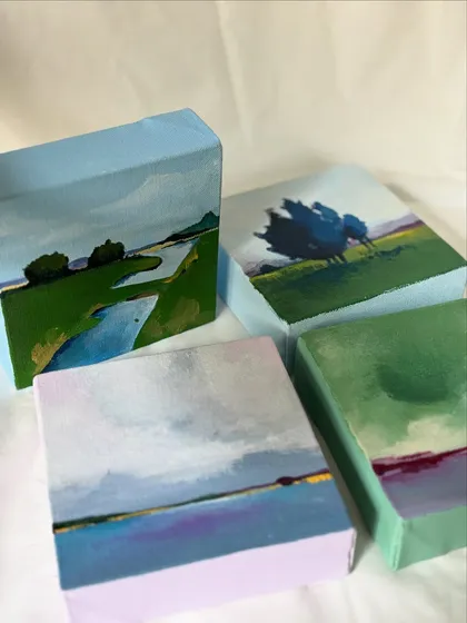 A group of four miniature landscape paintings, showing the wrapped edges of the canvas which are also painted to continue the scene.