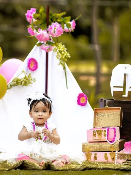 A candid moment from an outdoor first birthday shoot, where the birthday girl is taking a break from her cake to play.