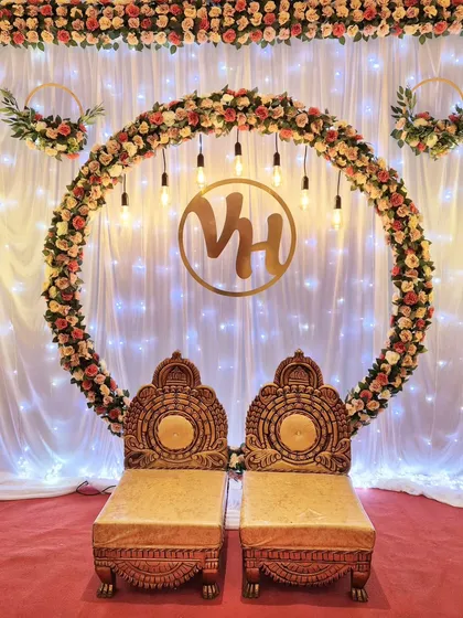 I designed this elegant engagement stage with a large floral ring of artificial roses, warm Edison bulb lighting, and a custom gold monogram for the couple. The traditional chairs complete this beautiful setup for a ring ceremony.