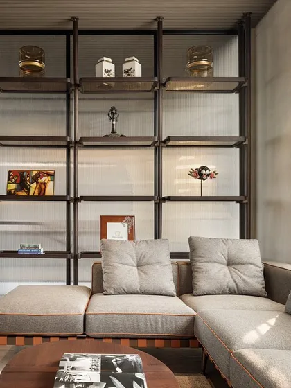 This executive lounge is designed for both work and rest, featuring a comfortable sectional sofa and a custom metal shelving unit. The space is separated by a glass partition, maintaining a sense of openness.