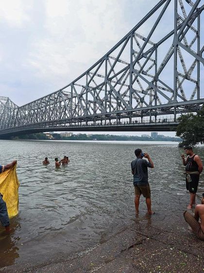 The daily life unfolding on the banks of the Hugli river in Kolkata, with the iconic Howrah Bridge in the background.