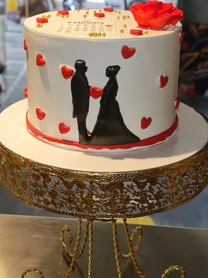 Celebrate a lifetime of love with this anniversary cake. It features a romantic silhouette of a couple, surrounded by hearts, and is topped with an edible calendar marking the special day.