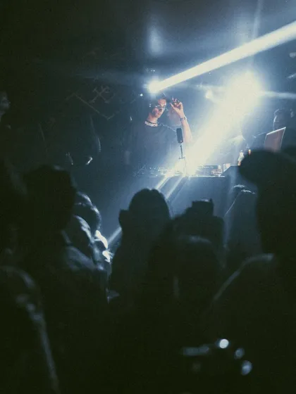 A grainy, atmospheric shot from the dance floor, looking up at me in the booth during a throwback hip hop night.