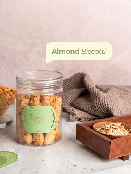 A jar of my Almond Biscotti, beautifully styled next to a wooden tray and a kitchen towel. It represents the simple, homemade goodness I stand for.