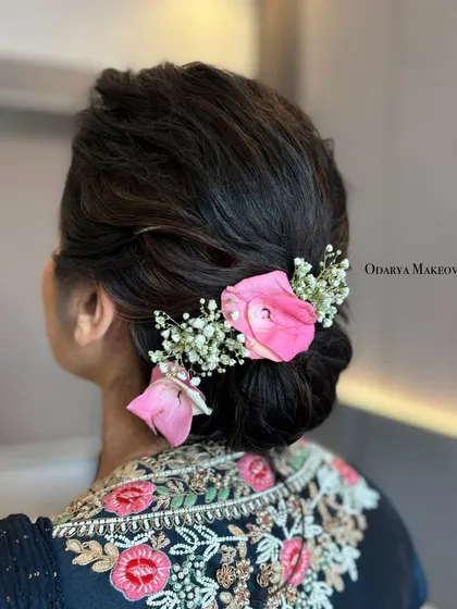 An elegant low bun adorned with a simple arrangement of a pink rose and baby's breath. This is a perfect example of how a minimalist accessory can create a sophisticated look.