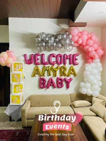 We can transform your living room into a festive space for your baby's arrival. This setup for 'Amyra' includes a custom balloon arch in pink, white, and silver over the sofa, along with our popular transparent 'B-A-B-Y' boxes.