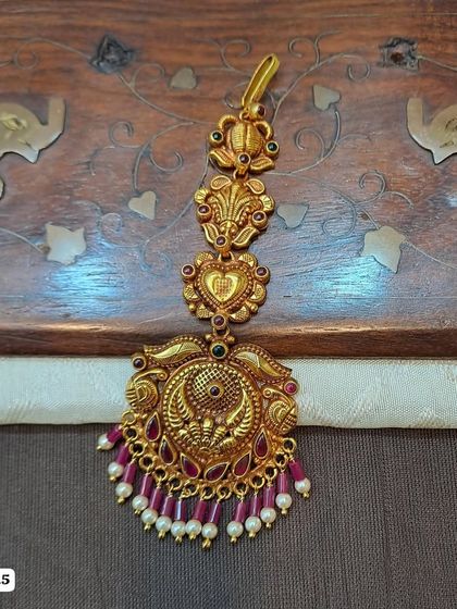 A lovely maang tikka with a peacock and floral design, made from 92.5 silver with gold plating. The ruby-colored bead drops add a touch of vibrant color.