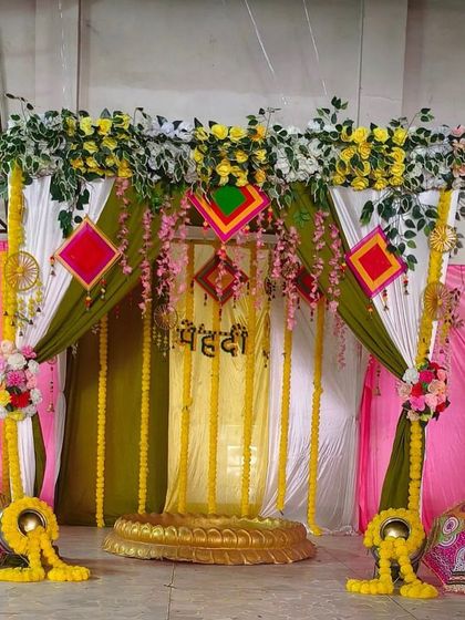 This Mehendi stage combines olive green and white drapes with hanging marigold garlands. The setup is framed with floral arrangements and includes traditional elements like Rajasthani hangings and umbrellas.