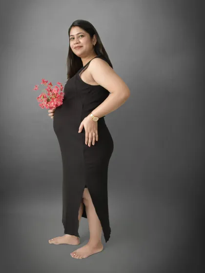 A simple yet elegant full-length portrait in a black maxi dress. The addition of a small bouquet of pink flowers adds a delicate touch of color and softness to this classic studio shot.