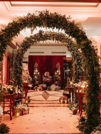 An enchanting entrance for a cocktail event, with lush green arches leading into a warmly lit, vintage-inspired space.