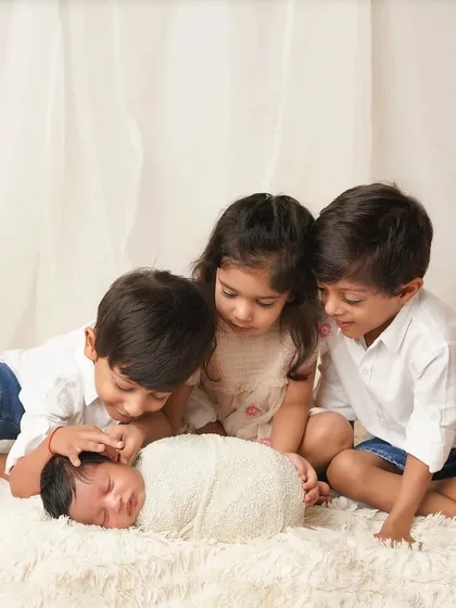 Three older siblings gather around their new baby brother, looking on with love and curiosity. Capturing the first meeting of the "crew" is always a special honor.