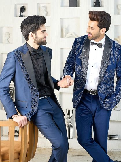 Two models share a lighthearted moment in my cocktail blue suits, showing that high fashion can also be about connection and shared style.