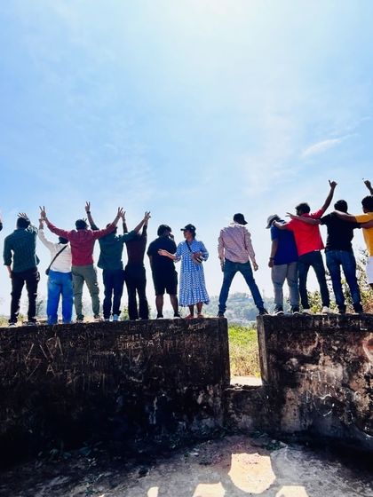 The group celebrating on top of an old fort wall in Coorg, with arms raised in joy.
