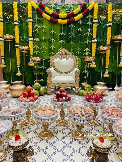 For a truly traditional Gruha Pravesha or Seemantham, a backdrop made of fresh banana leaves is perfect. Here, it's paired with yellow marigold garlands, brass pots, and a full display of fruits and sweets.