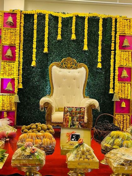 A complete Seemantham stage with a vibrant backdrop and a full display of offerings. The decor uses a bright color palette of yellow, magenta, and green, creating a joyful atmosphere.