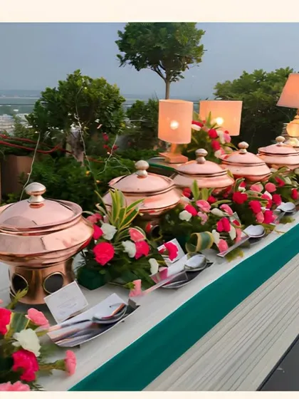 A rooftop buffet line featuring traditional copper chafing dishes, fresh floral arrangements, and table lamps for warm evening ambiance.