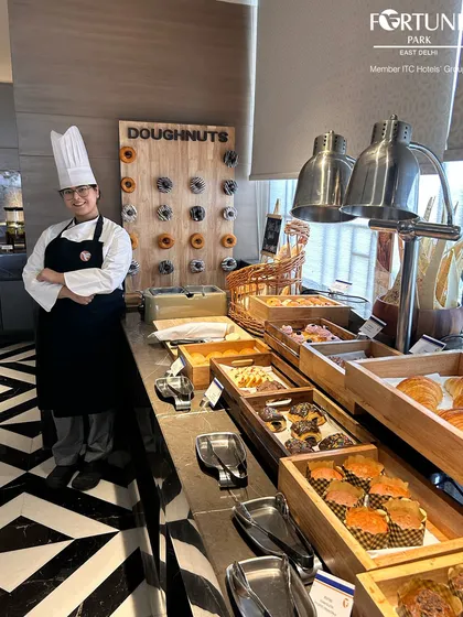 One of our talented chefs standing proudly by the pastry and doughnut wall, a popular feature of our breakfast buffet.