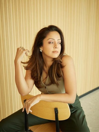 A seated portrait that highlights the delicate pearl earrings and the casual elegance of the waistcoat.