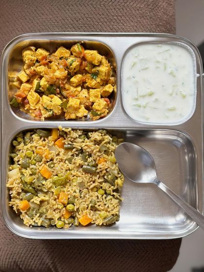 A delicious meal of vegetable pulav with paneer bhurji and a side of cucumber raita.