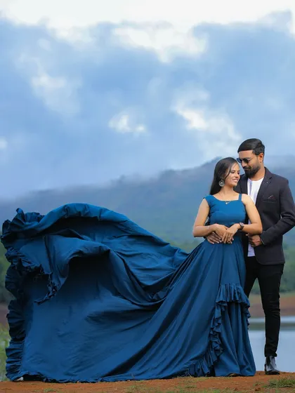 A stunning pre-wedding shot by the lake. The massive blue trail of the gown creates a dramatic "flying" effect against the mountain backdrop.