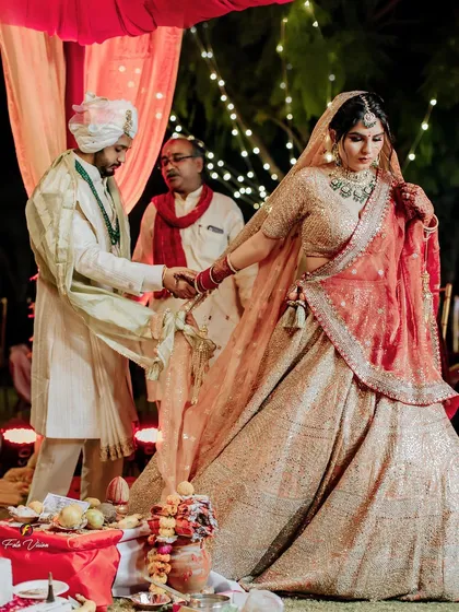The couple performing the phera ceremony, a central ritual of their Hindu wedding, captured in the warm glow of the sacred fire and ambient lights.