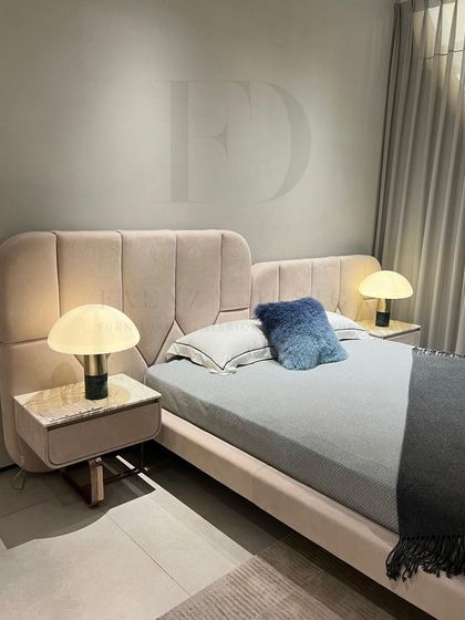 Soft and inviting, this bedroom features a bed with a channel-tufted, curved headboard in a dusty pink velvet. The matching bedside tables with marble tops and mushroom lamps complete the gentle, elegant look.