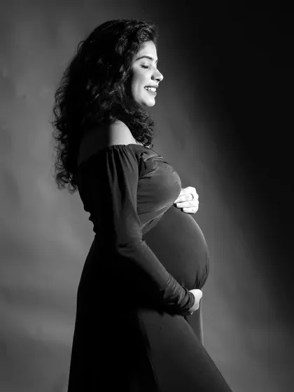 A joyful black and white solo portrait. The side lighting beautifully highlights the mother-to-be's smile and baby bump.