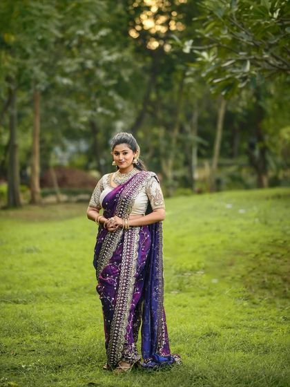A classic portrait in a lush green park, the purple saree stands out beautifully against the natural backdrop.