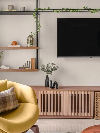 A close-up of the TV console in the "Zen Residence," featuring slatted wood doors and a woven basket for texture. The open shelving above is styled with greenery and books, adding a personal touch.
