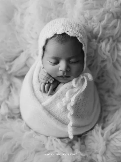 Simplicity is timeless. A newborn wrapped snugly in a white bonnet and swaddle, resting on a soft fur rug. This clean, classic look will never go out of style.