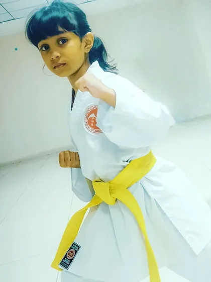 A young girl in a yellow belt holds a strong fighting stance. We empower our students with the confidence that comes from mastering fundamental karate postures.